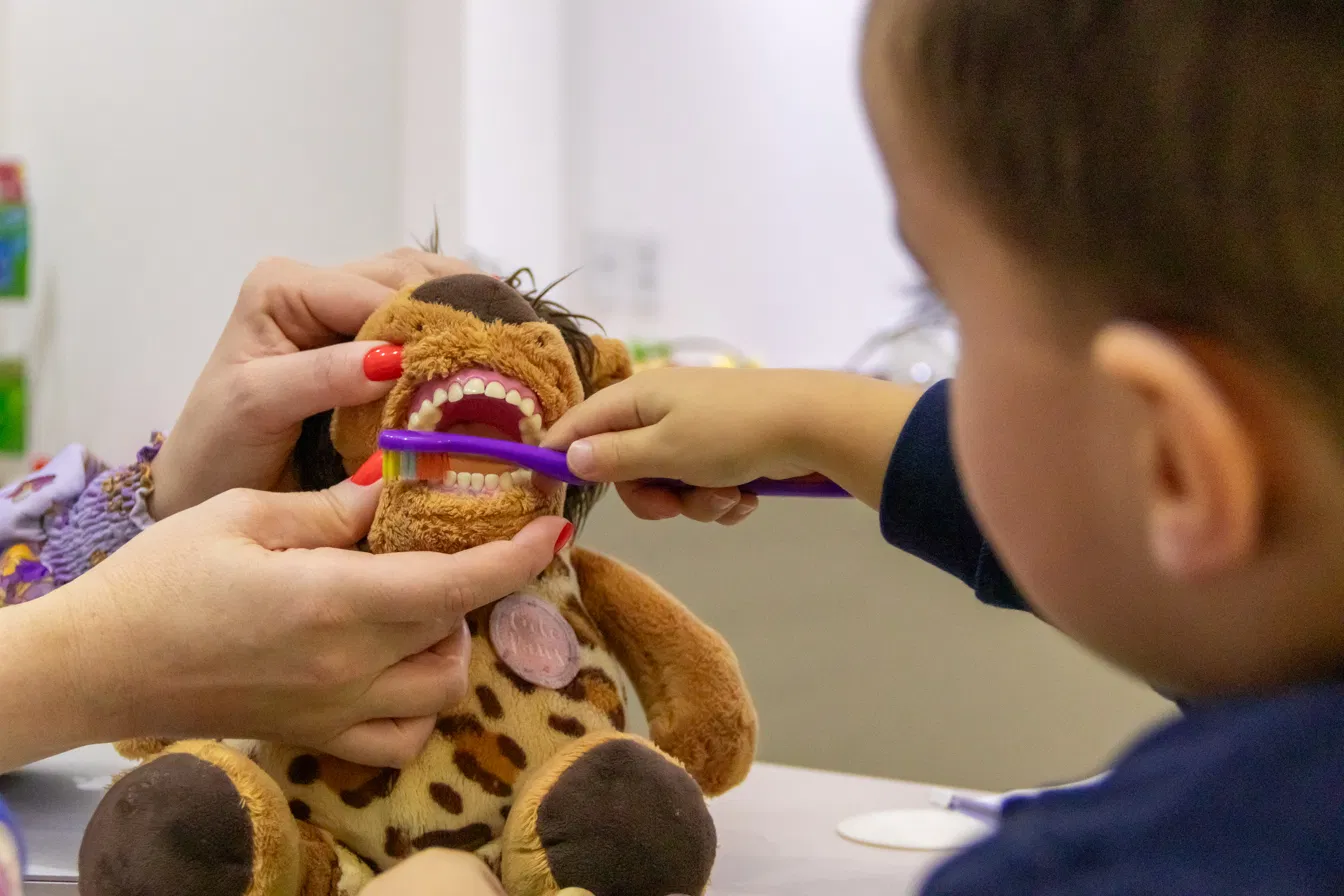 Criança escovando os dentes do leãozinho de pelúcia